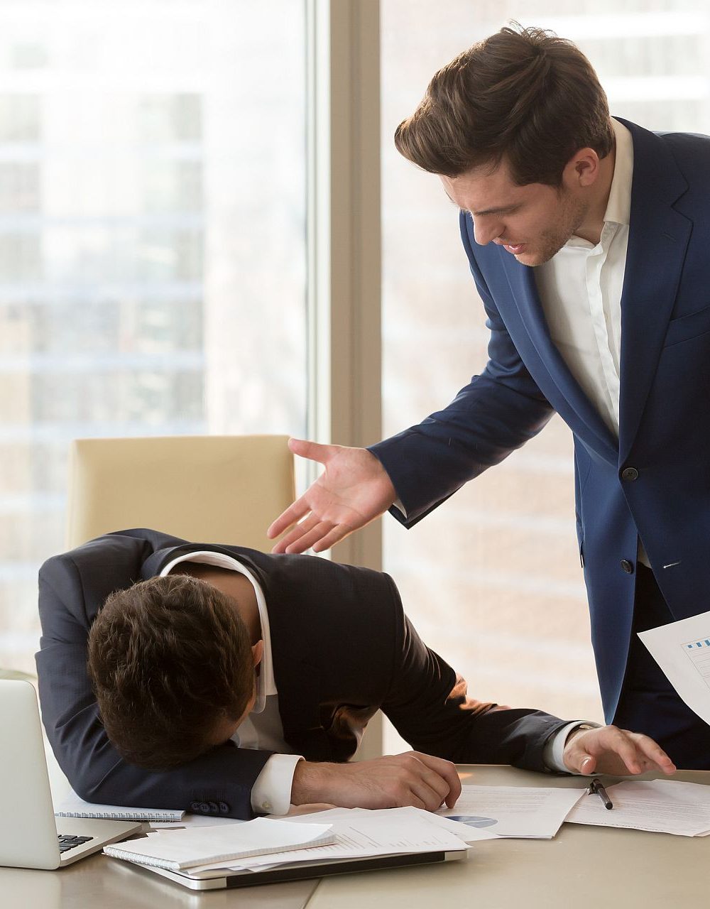 Bad angry boss yelling at male sad depressed employee, lying with face down on office desk, ineffective worker made mistake receiving reprimand from team leader, scolding for failure, missed deadline